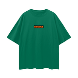Green FNDMNTLS. Shattered Tee with bold orange logo on chest, oversized unisex cotton t-shirt with deep drop shoulders for casual style.