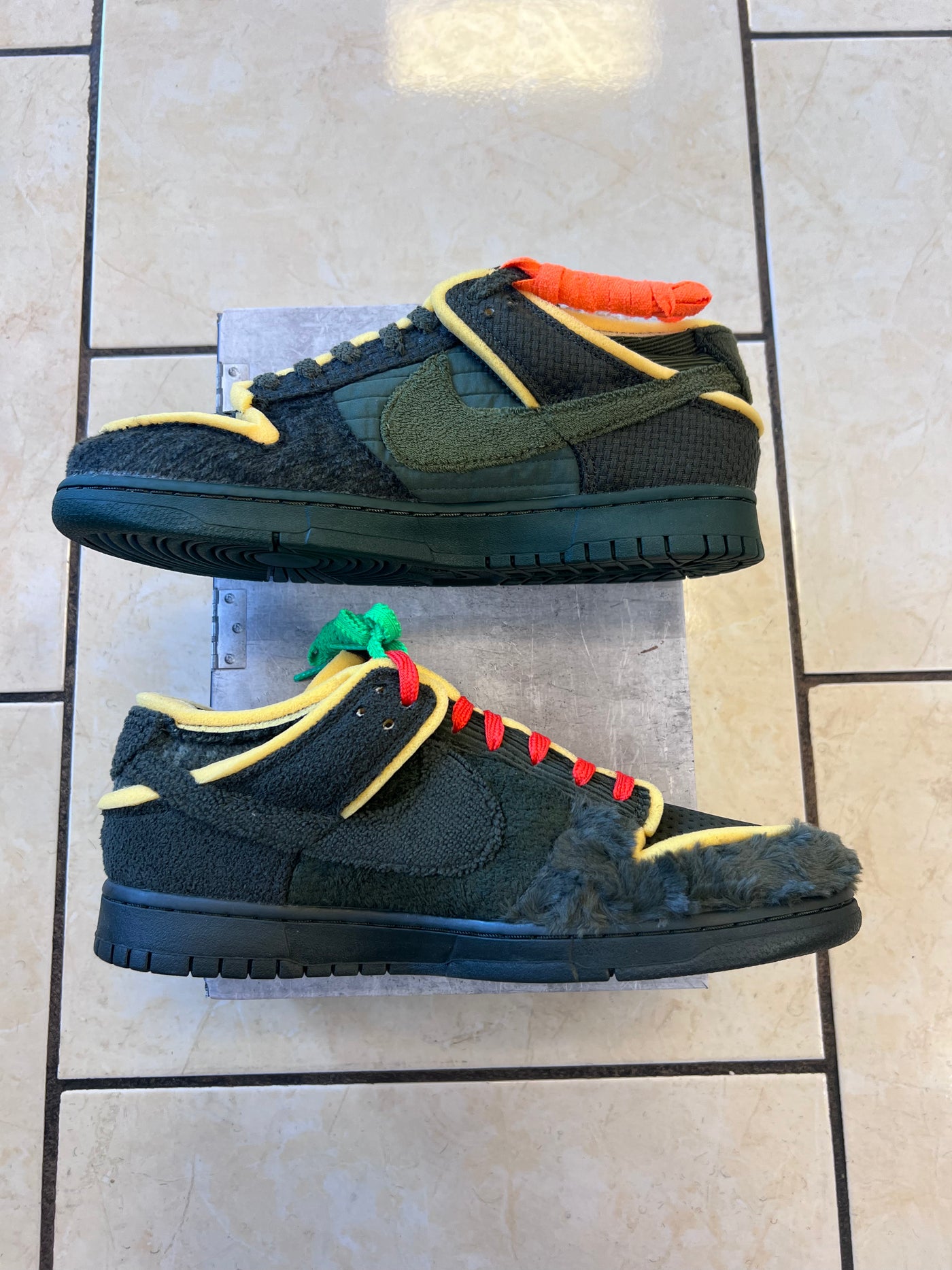 Pair of black and green sneakers with colorful accents on a tiled floor.