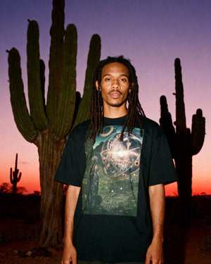 Ezekiel 1:4-28 Cotton T-Shirt - Unisex features a vivid biblical print on black cotton, worn by a model standing in a desert at sunset with cacti.