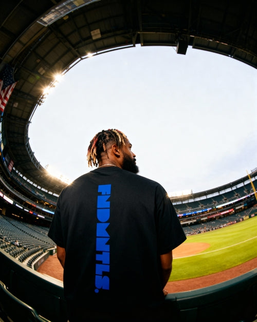 Back view of black Mets Blue T-Shirt - Heavyweight Earth Tone with vertical blue FNDMTLS logo. Styled for stadium streetwear.