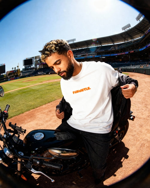 White Mets Orange Heavyweight T-Shirt styled with black jacket on motorcycle, featuring orange FNDMTLS logo for streetwear look.