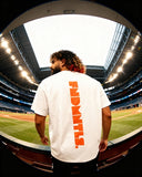 Back view of white Mets Orange Heavyweight T-Shirt with bold vertical FNDMTLS print, worn at stadium for casual unisex fashion.