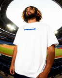 Mets Blue T-Shirt - Heavyweight Earth Tone in white with bold FNDMTLS logo, worn at a baseball stadium. Unisex cotton casual streetwear.